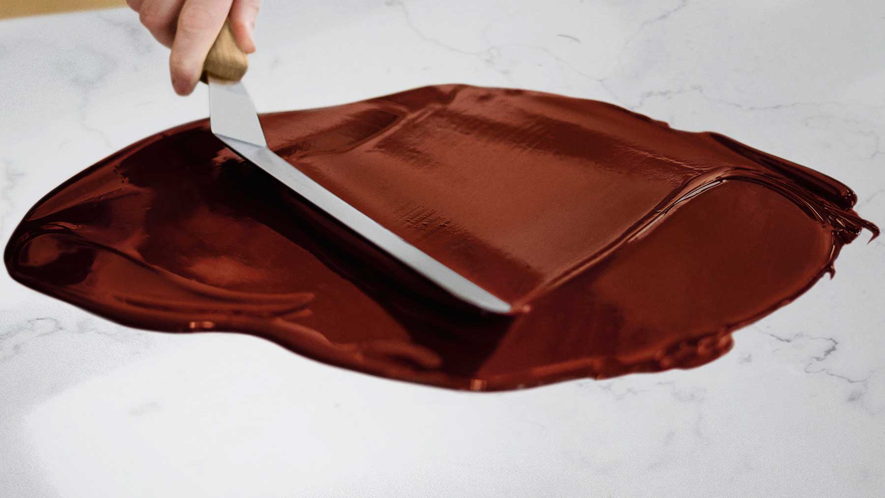 A cook uses a spatula to spread melted Dove Chocolate onto a marble surface