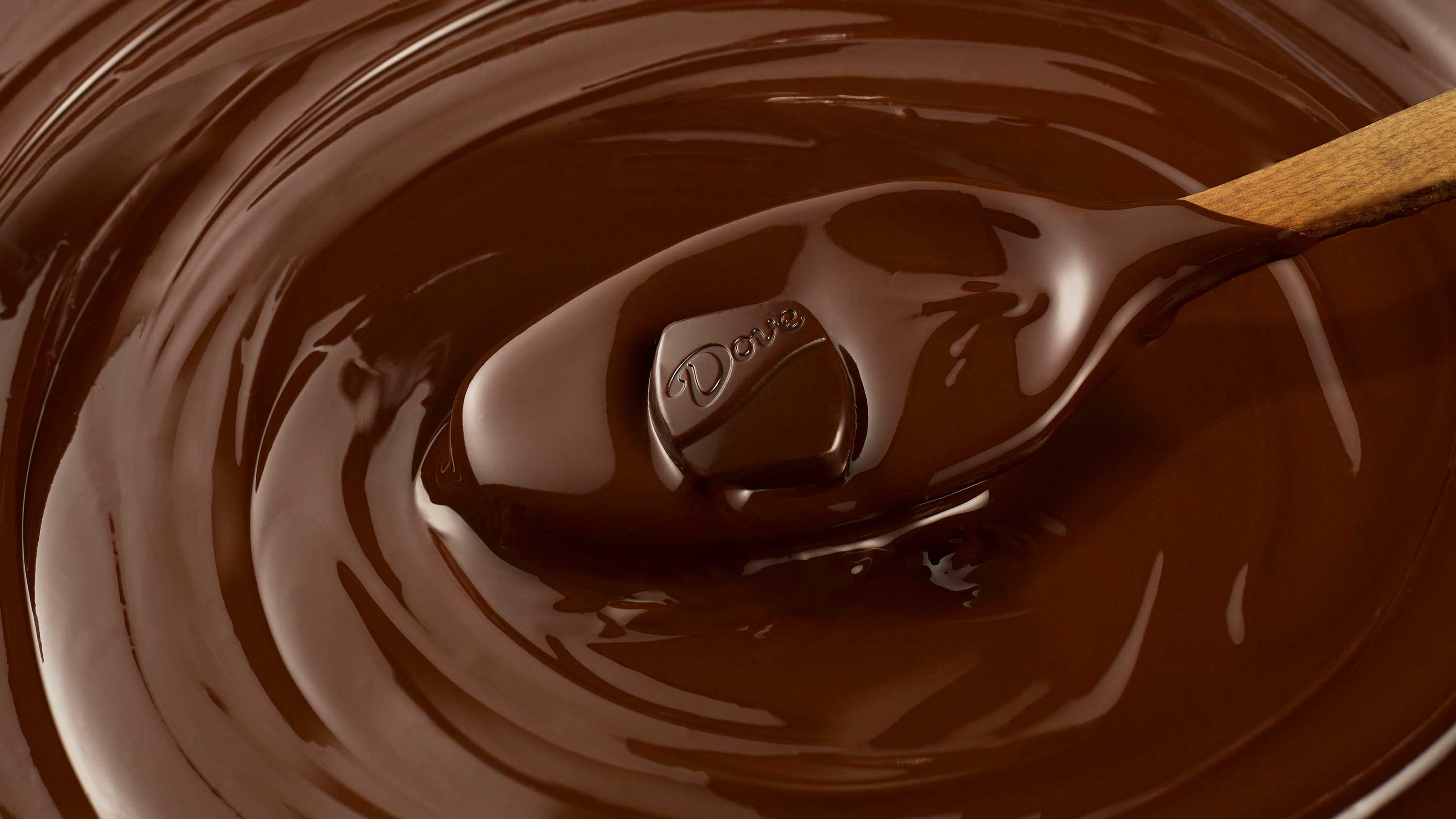 A photograph of a Dove Promise Candy being lifted out of melted chocolate.
